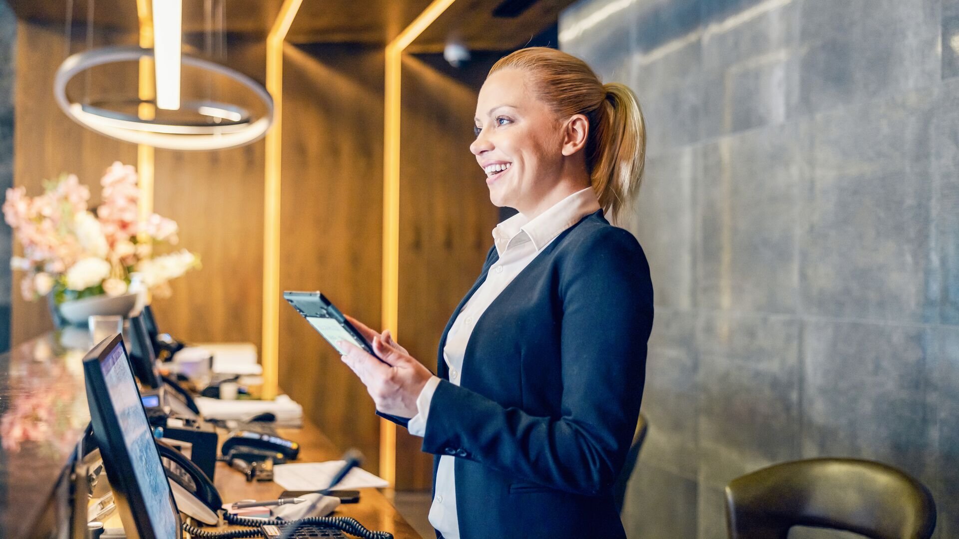 UK_Large-A happy receptionist is talking with guest and keeping a tablet.